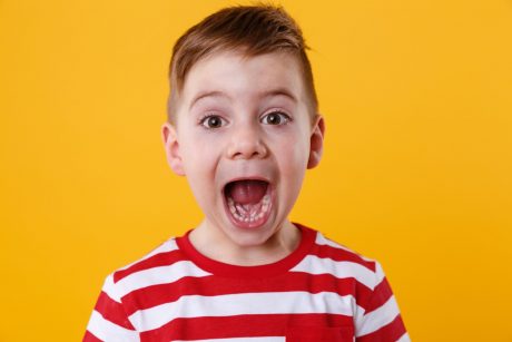Close up portrait of a little boy screaming out loud isolated over orange background
